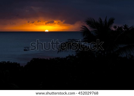 Bright orange sunset looking out to see in a tropical paradise, with boats moored in a bay.