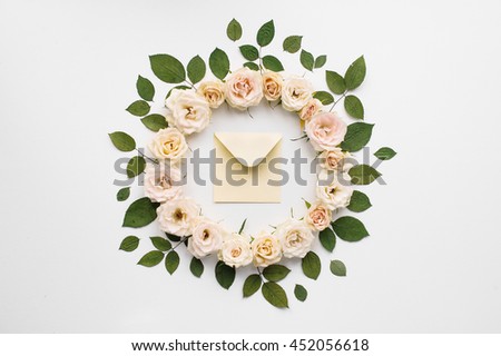 Wreath of pink roses and green leaves with envelope in centre isolated on white background, flat lay, overhead view, wreath frame with pink and tea roses