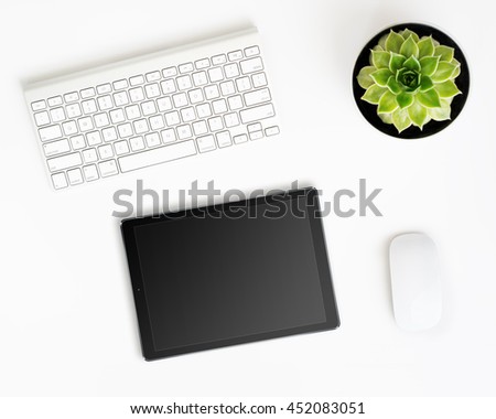 White office desk table with tablet pc computer in ipade style with black screen, wireless aluminum keyboard, mouse and succulent flower in pot. Top view with copy space. Flat lay. Royalty-Free Stock Photo #452083051