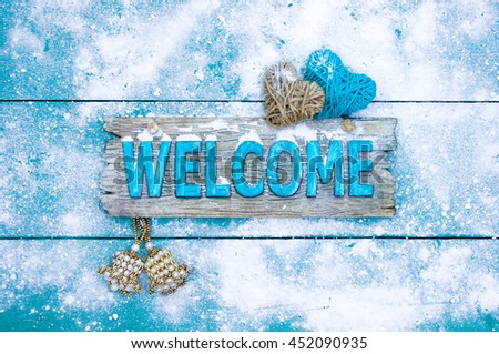 Winter holiday welcome sign with rope hearts,bells and snow hanging on antique teal blue wood background; Christmas concept