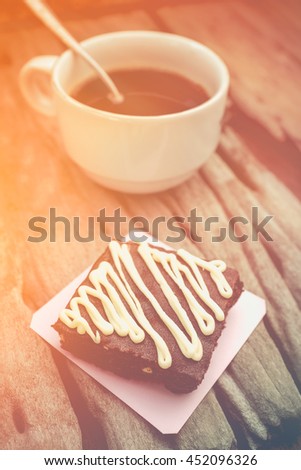Piece of cake chocolate brownie and hot coffee on old wooden background with sunlight. Shallow depth of field (dof), selective focus. Warm tone and vintage picture style.