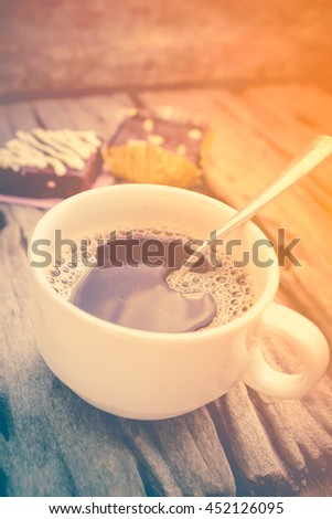 Hot coffee and cake chocolate brownie on old wooden background with sunlight. Shallow depth of field (dof), selective focus. Warm tone and vintage picture style.