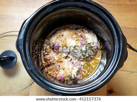 Pulled pork meat cooking in crock pot or slow cooker, with a wooden background. Viewed from above. Royalty-Free Stock Photo #452157376