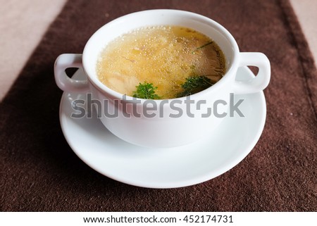 Chicken broth with herbs served in a white bowl top view
