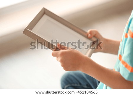 Child's hands holding photo frame on light background
