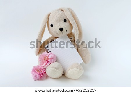 little rabbit toys holding blank notebook on white background 