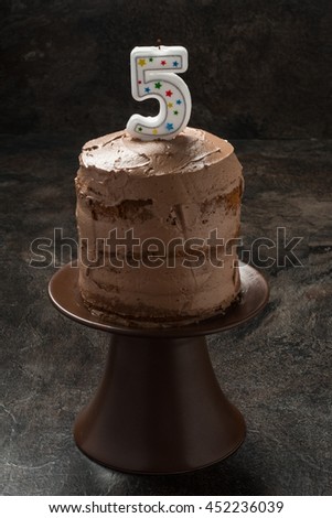 Three layer chocolate cake with icing and candle on brown background
