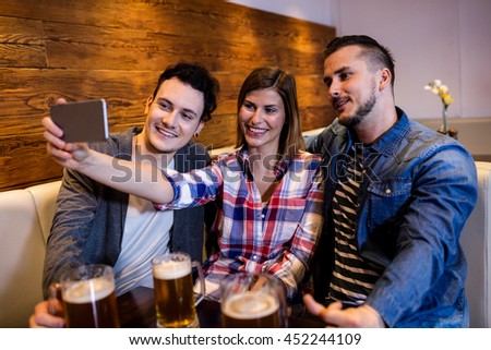 Happy friends taking selfie through mobile phone at restaurant