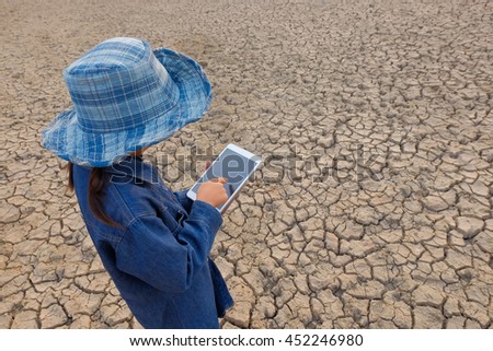 a selective focus picture of a laptop in young farmer's hands on dried cracked land  