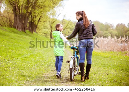 Daughter and mother walk along the shore of the lake in spring Park with a bike and talk. Family values, education.A photo from the back