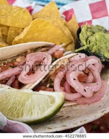 A fish taco on a plate with chips,salsa and guacamole.