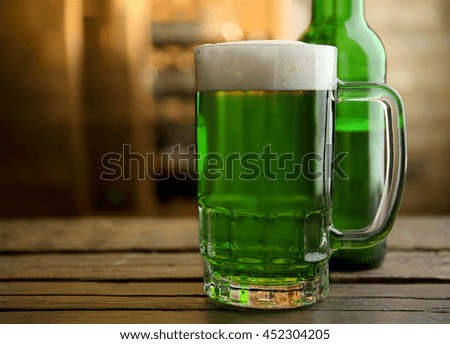 Glass of green beer and bottle on blurred bar background
