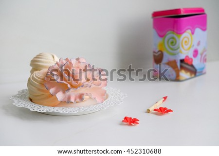 white plate with round orange colored marshmallows and edible pink rose bud near on table red small flower bloom and wooden stick for paint, on background blurry vivid colored metal box/object replace