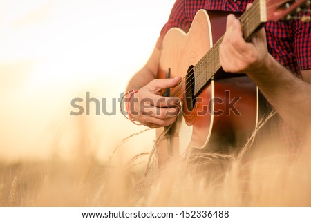 Close up of male hands playing acoustic guitar on the wheat field at the sunset. Retro, music, lifestyle concepts. Royalty-Free Stock Photo #452336488