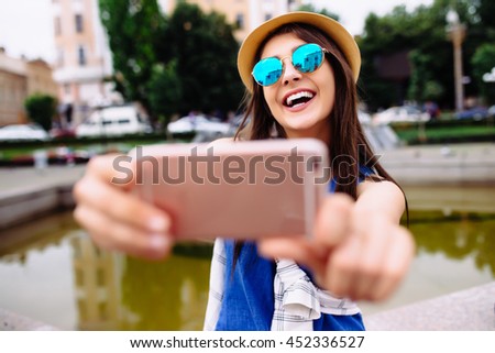 Young smiling teen happy woman making selfie on the street, glasses, traveling alone, having fun, positive mood, joy, vacation, surprised emotions. Urban life concept.