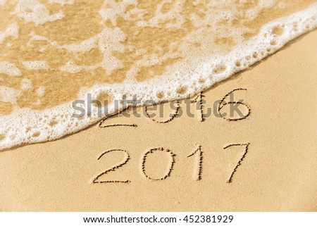 2016 2017  inscription written in the wet yellow beach sand being washed with sea water wave. Concept of celebrating the New Year at some exotic place