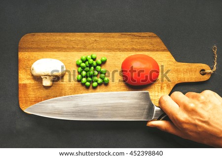 Fresh products are neatly on a wooden cutting board and woman hand with a bid kitchen knife