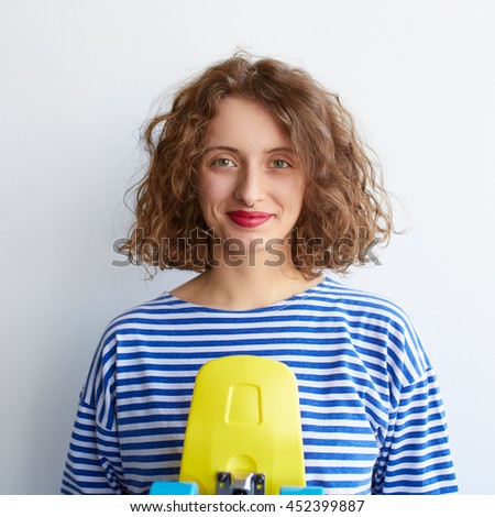 Hipster girl holding a yellow color skateboard over white background. Curly cute young woman with penny board