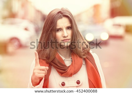 Attention! Closeup portrait head shot confident angry serious young girl business woman showing index finger for admonition isolated cityscape outdoor background. Multicultural mixt race asian russian