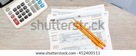 USA IRS tax form 1040 for year 2015 with pencils and calculator with a laptop keyboard on wooden desk. Sized to fit a popular social media cover image placeholder