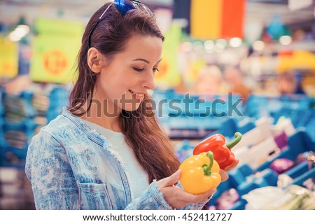Closeup portrait, beautiful, pretty young woman picking up, choosing bell peppers vegetables in grocery store supermarket 