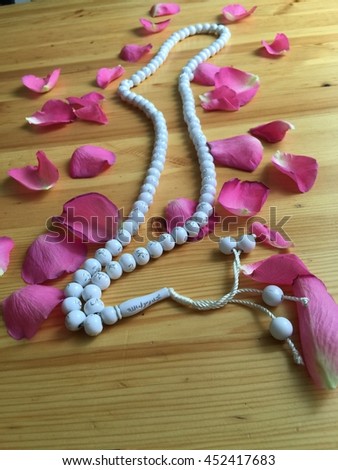 White islamic rosary beads with pink roses leaves on the wooden background. Muslim photography