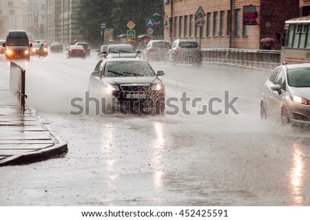 High speed. Moving car sprays puddle when heavy rain drops on concrete. Motion picture. 