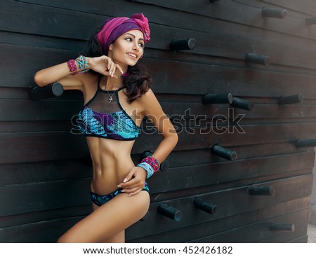 Fashion photo of beautiful tanned woman with perfect body and hair in bikini posing in sunny day over the wall.Sensual young girl enjoying vacation on luxury villa. Colorful filter,tan skin tone Royalty-Free Stock Photo #452426182