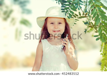 Kid with smartphone. Closeup portrait of pretty smiling funny girl kid holding cell phone  just had a pleasant conversation with her family outdoors summer background. Kids and technology concept