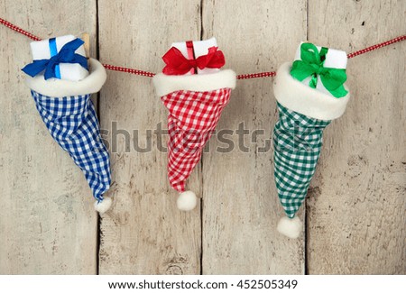 Three checkered santa hats filled with christmas gifts hanging in front of a rustic wooden wall, parcels