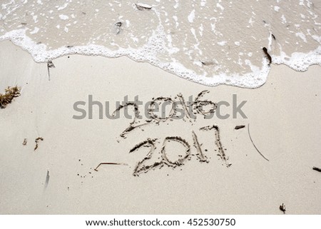 New Year 2017 is coming concept.  2016 and 2017 written on a beach sand, the wave is almost covering the digits 2016 Royalty-Free Stock Photo #452530750