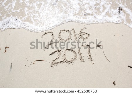New Year 2017 is coming concept.  2016 and 2017 written on a beach sand, the wave is almost covering the digits 2016 Royalty-Free Stock Photo #452530753