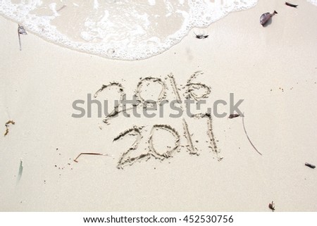 New Year 2017 is coming concept.  2016 and 2017 written on a beach sand, the wave is almost covering the digits 2016 Royalty-Free Stock Photo #452530756