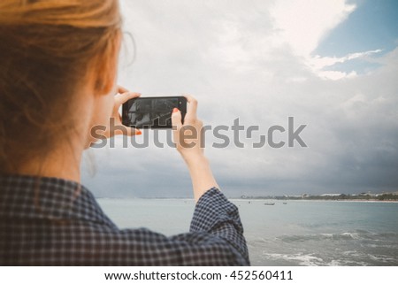 Woman taking photos of the beach with cell phone during the 