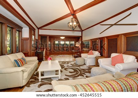 Luxury Living room interior with brown wooden trimmings, vaulted ceiling and beams. White sofa set and armchairs with pink pillows create comfort atmosphere.