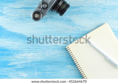 blank notebook with a ballpoint pen and old vintage photo camera on blue wooden background. Mock up. Top view. Flat lay.