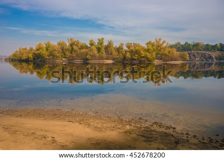 River landscape in autumn, view from one side of the beach sand  on the blue mirror surface of the river and the other side with a band of colorful trees