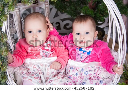 Funny twins in pink dress sitting in a white wicker basket on a winter New Year's background. Beautiful happy kids