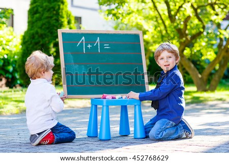 Two siblings children at blackboard practicing math, outdoor school or nursery. Happy kid boys counting and having fun together.
