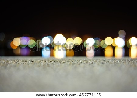 Focus on cement pier and Abstract blurred night view of city wharf lights, and inverted reflection in water and coastline skyline as background.