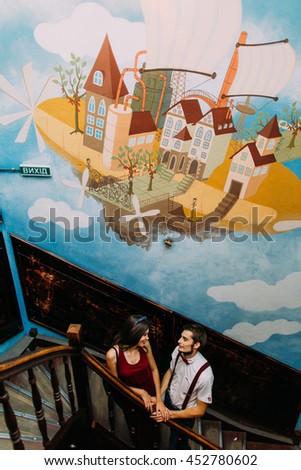 Couple in love holding hands at the old wooden staircase. Creative bright cartoon mural on wall background