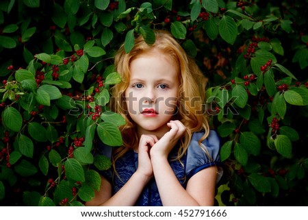 Portrait of beautiful little girl in a blue dress on a background of leaves cherries