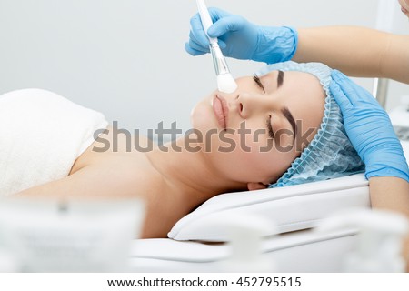 Model lying on couch with closed eyes. Hand in blue glove touching patient's face with brush. Cosmetological clinic. Healthcare, clinic, cosmetology Royalty-Free Stock Photo #452795515