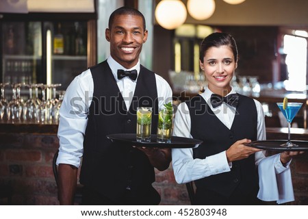 Portrait of waiter and waitress holding a serving tray with glass of cocktail Royalty-Free Stock Photo #452803948