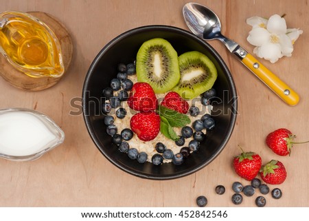 Breakfast with oatmeal, nuts, fruit, kiwi banana, berries, strawberries, blueberries, cinnamon, honey and milk stands on a wooden table