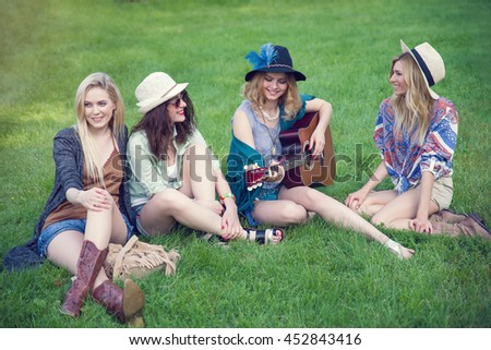 Four young women, girlfriends. Girls wearing boho style. Hippie woman with guitar. Group of women spending time outdoors.