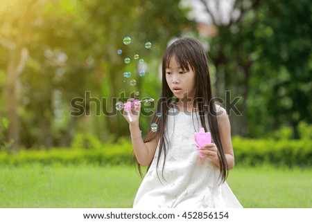 A little happy girl blowing soap bubbles in summer park. 