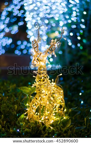 Blurred yellow light of reindeer shape decoration idea for christmas celebration on green grass with blue bokeh light for the beautiful background