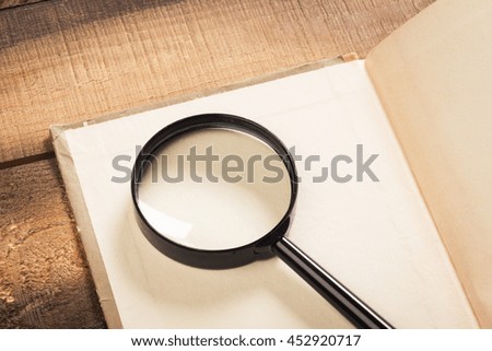 Magnifying glass and book o the wooden background