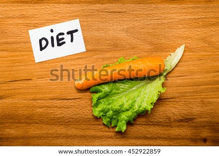 Wet lettuce with carrot and a card with the word "DIET"on wooden table. Close-up view from above